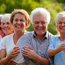 Grupo de adultos mayores riendo y conversando en un parque, simbolizando conexiones sociales.